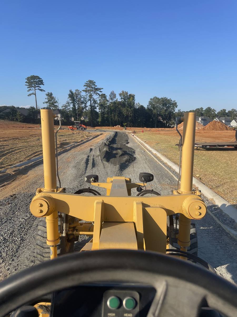 Motor grader spreading stone base on a new street, seen from the cab